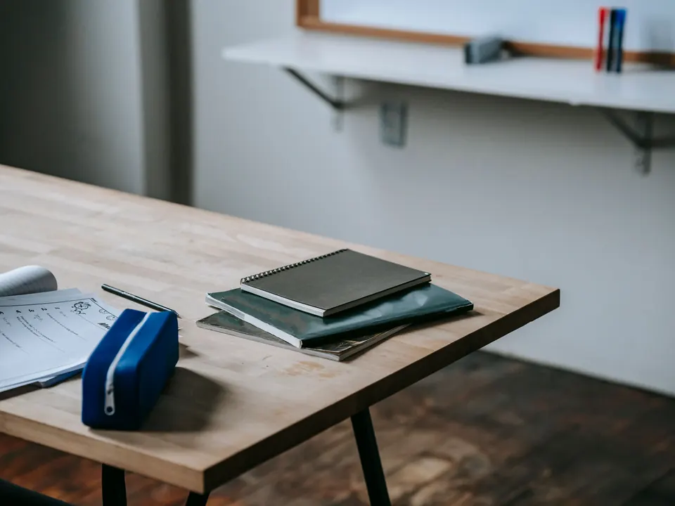 Houten tafel met schriften, een etui en een werkblad in een leeg lokaal