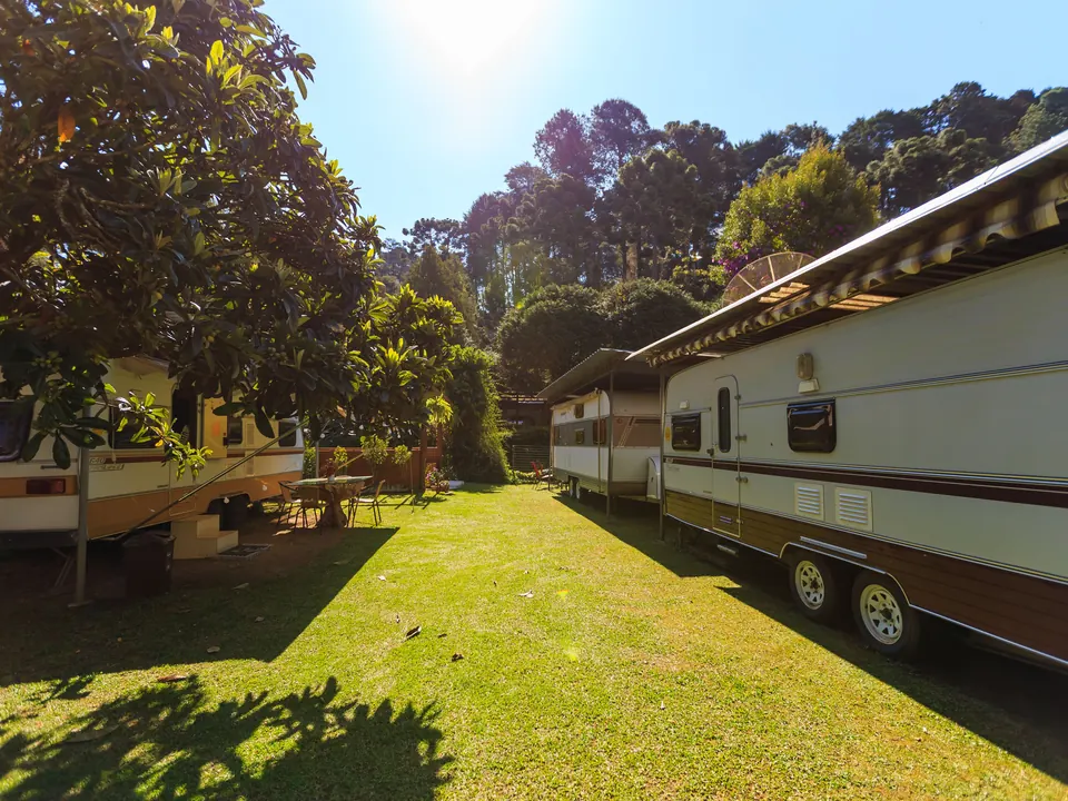 Zonnig grasveld op een camping met caravans onder bomen en een tafel met stoelen