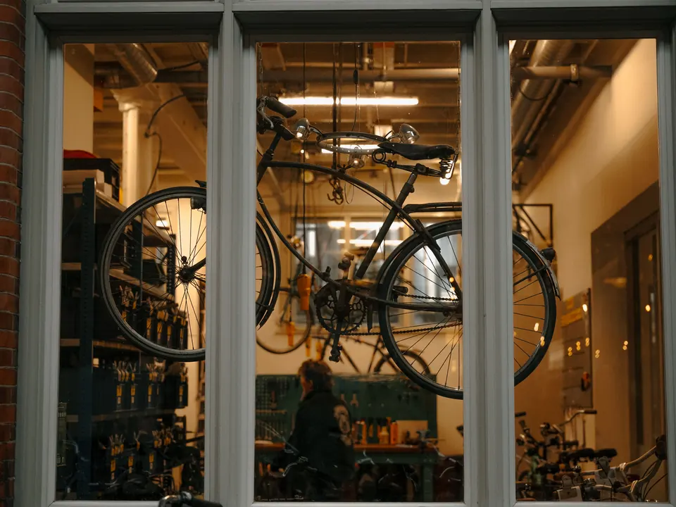 Fietsenwerkplaats gezien door een raam, met een fiets aan het plafond en gereedschap op de achtergrond