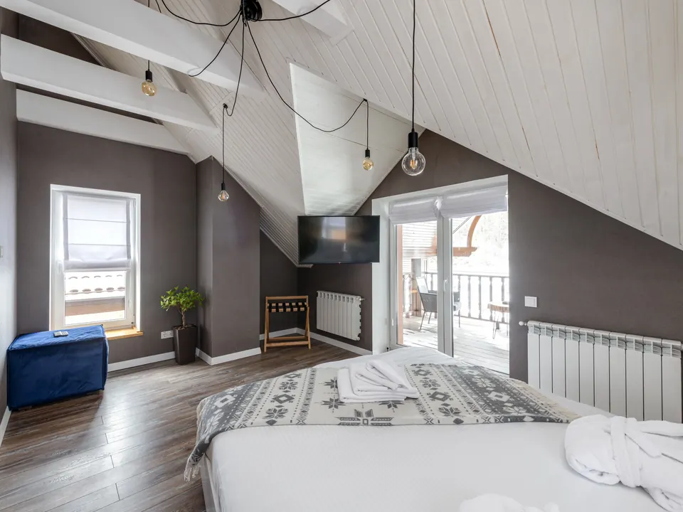 Hotelkamer onder een schuin dak met een groot bed, handdoeken en badjas en een balkondeur