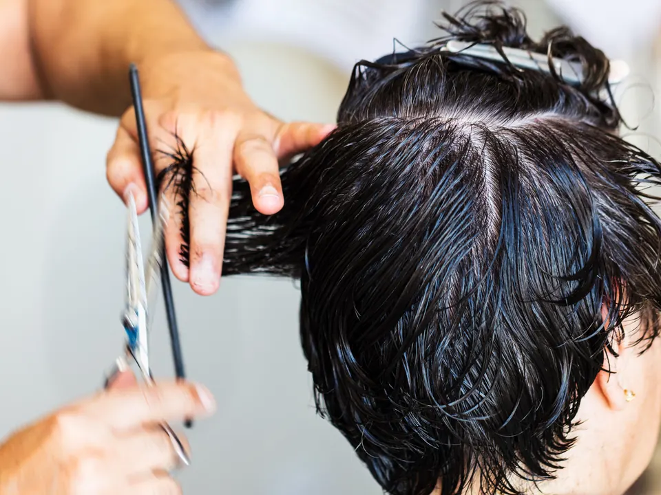 Kapper knipt natte donkere haren met schaar en kam, zonder herkenbaar gezicht