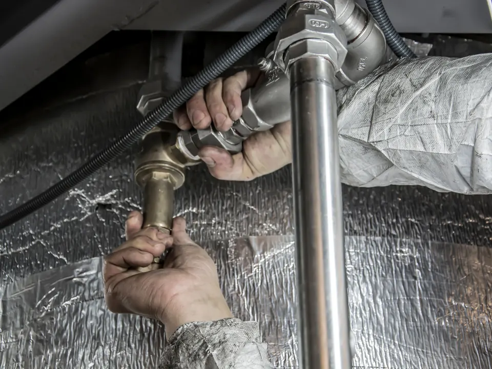 Handen van een loodgieter die metalen leidingen en een kraan onder een gootsteen vastzetten