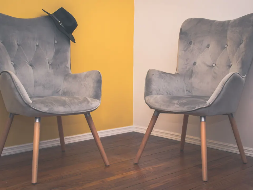 Twee lege grijze fauteuils die naar elkaar toe staan in een hoek met een gele en een witte muur