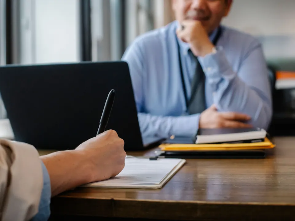 Sollicitatiegesprek aan een houten tafel met laptop, notitieblok en dossiermappen