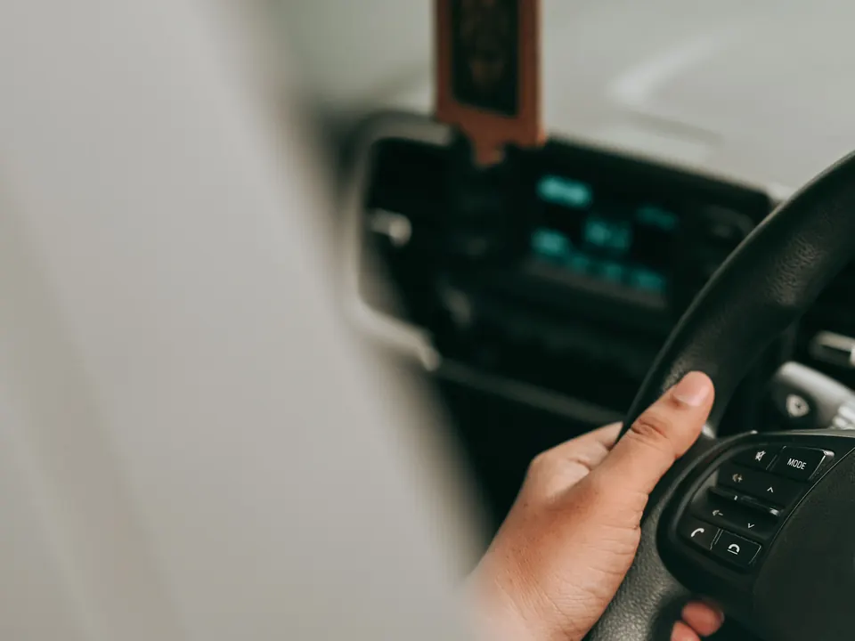 Hand aan het stuur van een auto met het dashboard op de achtergrond