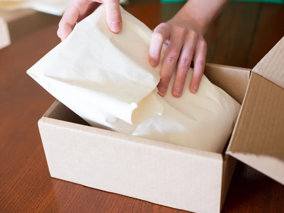 Handen wikkelen een product in papier in een kartonnen verzenddoos
