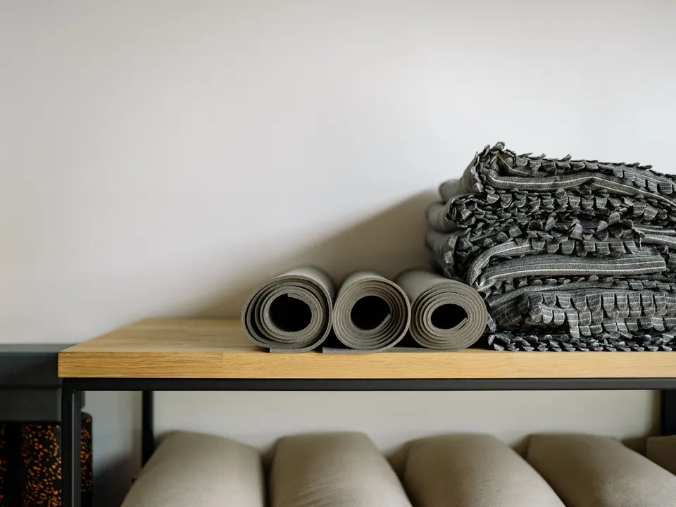 Opgerolde yogamatten en gevouwen dekens op een houten plank in een rustige studio