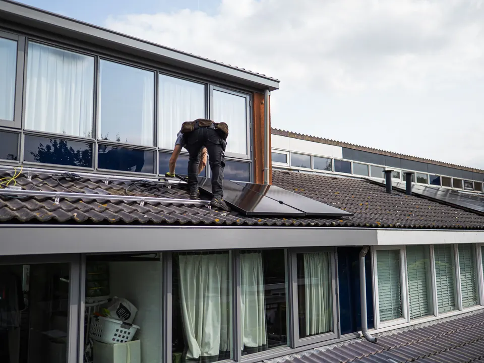 Monteur legt zonnepanelen op een pannendak van een woning
